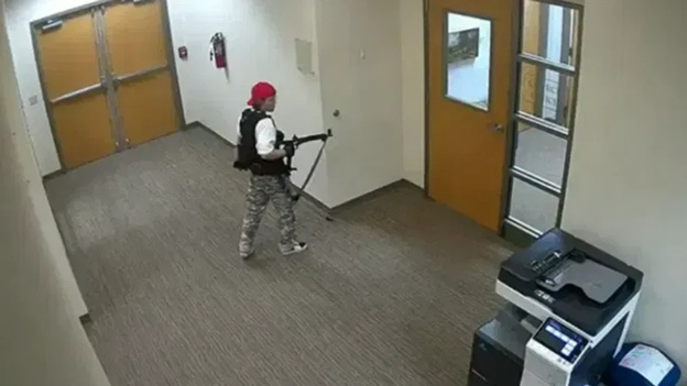 This picture shows a young adult carrying an automatic weapon in a school.