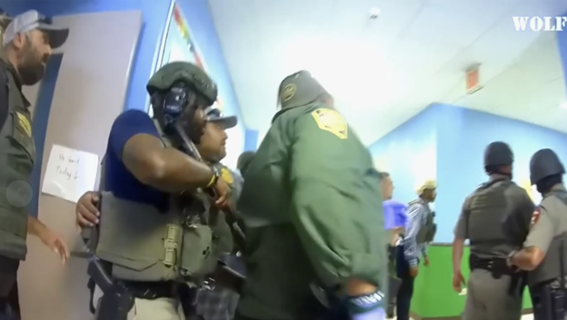 This is an image of a police officer's camera showing multiple officials in a school hallway with weapons drawn.