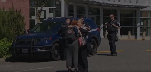 two woman hugging with a uniformed cop in background