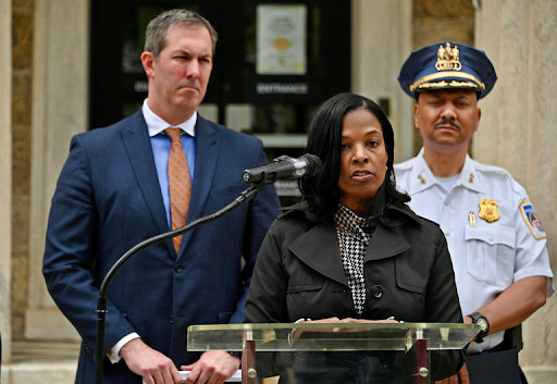 woman in black jacket at microphone with two men standing behind her